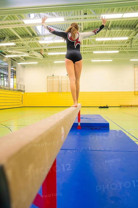 Female athlete balancing on a balance beam in a bright yellow hall, Gymnastics, Calw, Germany