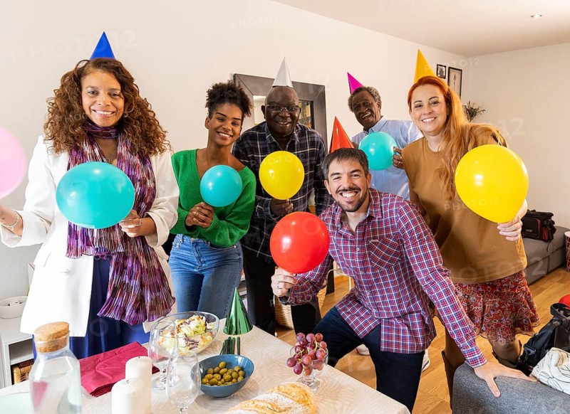 A joyful group of friends celebrating a birthday with colorful balloons and party hats indoors. Laughter and happiness fill the room, highlighting a festive occasion