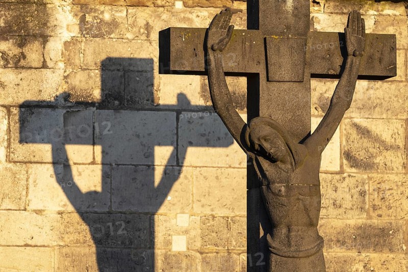 Stone cross with shadow cast at sunrise, cathedral cemetery near Cologne Cathedral, Cologne, North Rhine-Westphalia, Germany