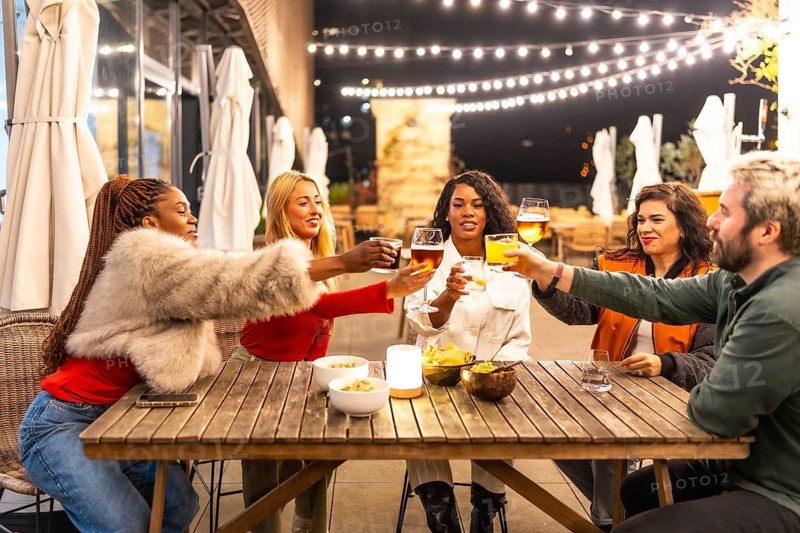A cheerful multi-ethnic group of friends toast drinks at a night-time outdoor dining event