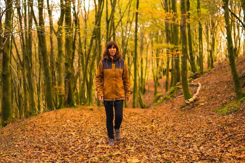 Lifestyle, a young woman in a yellow jacket walking backwards along a forest path in autumn. Artikutza Forest in San Sebastián, Gipuzkoa, Basque Country. Spain