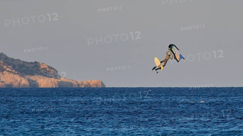 Wingfoiller, surfer jumping high over the sea with cliffs in the background in the evening light, windsurfer, Meltemi windsurfing spot, Devils Bay, Paralia Vatha, Vatha Beach, southeast coast, Karpathos, Dodecanese, Greek Islands, Greece