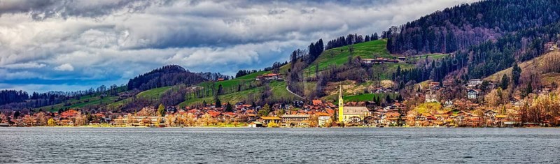 Picturesque village on the lakeshore with church, surrounded by green meadows and hills under a cloudy sky, Schliersee