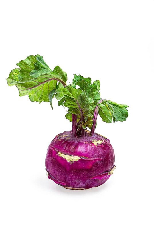 Fresh purple kohlrabi with vibrant green leaves displayed on a white background in a studio setting