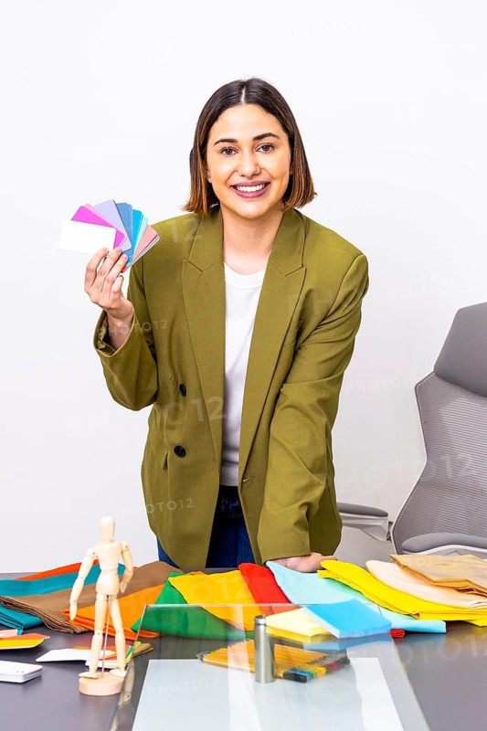 A professional woman of image consultant in a green blazer offers color palette advice in a modern office setting. The table is covered with vibrant fabrics and color samples