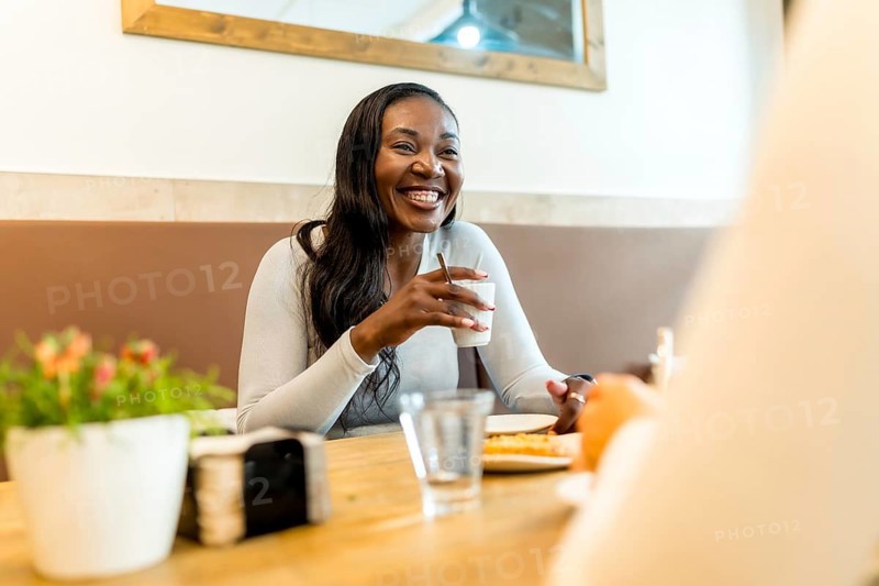 Happy customer smiling and holding a cup of coffee while chatting with a friend during a relaxing break at a modern cafe