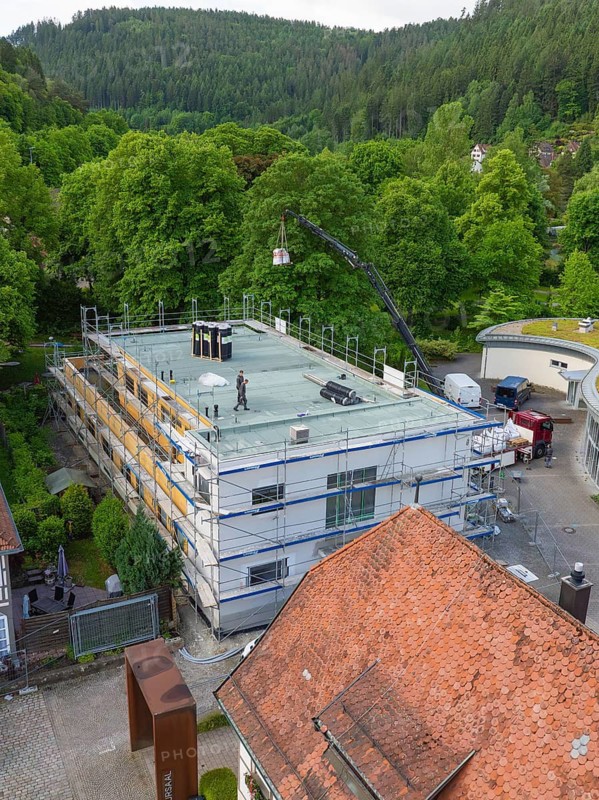 Workers carry out roof work on scaffolding, surrounded by forest and village, new building KITA Calw Hirsau, Black Forest, Germany