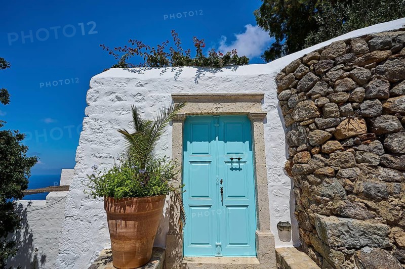 Turquoise-coloured door in a white building with a plant in a clay pot and a stone wall, Chora, main town of Patmos, Patmos, Old Town, Dodecanese, Greek Islands, Greece