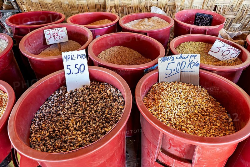 Red colored containers full of grains and legumes with price tags at a market stall, market and market stalls on the streets of Nasca in Peru