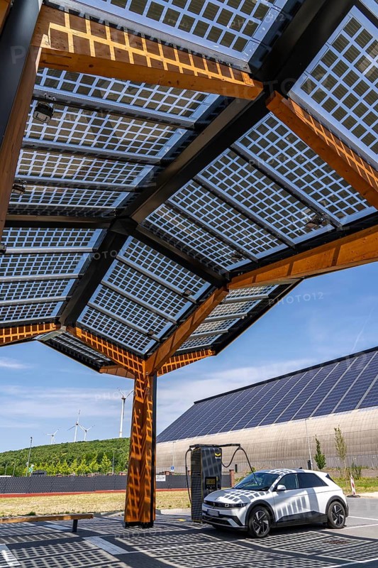 Electric charging station on the site of the former Lohberg colliery in Dinslaken, operated by Fastned, uses electricity from wind power and solar energy, fast-charging columns, with its own solar roof, in the background the 11, 500 square metre solar roof on the colliery's former coal mixing hall, wind farm on the Lohberg slagheap, North Rhine-Westphalia, Germany