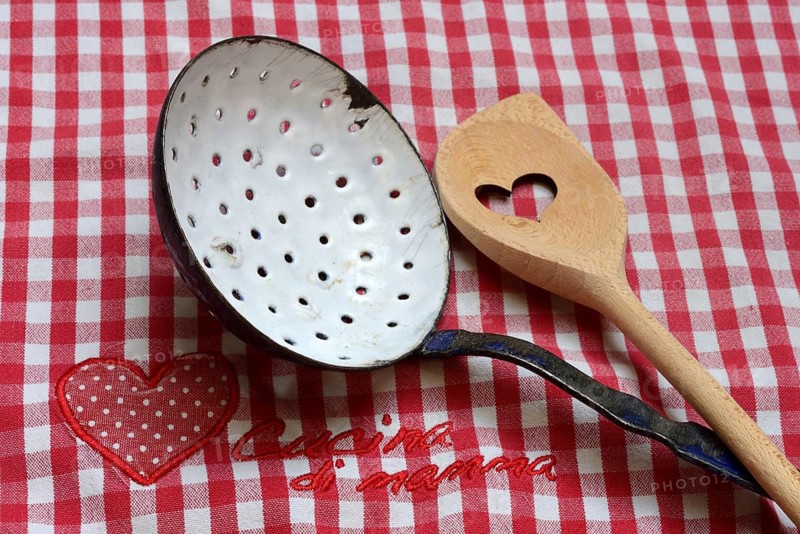 Dish drainer and cooking spoon on kitchen towel with lettering 'Cucina di mamma'