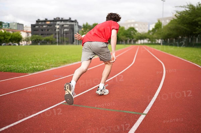 Full length rear view of a male caucasian young athlete leaving starting line in running track