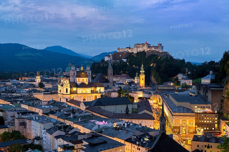 Evening lights of Salzburg with the majestic Hohensalzburg Fortress and the Alps in the soft twilight, Salzburg, Salzburger Land, Austria