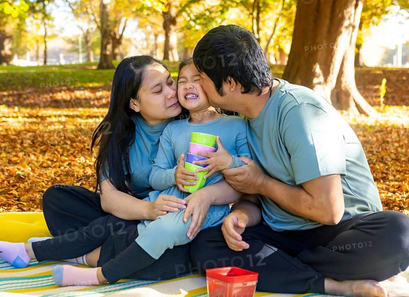 A joyful Asian family shares a warm embrace during an autumn picnic in the park. Surrounded by vibrant fall foliage, they enjoy time together with laughter and love