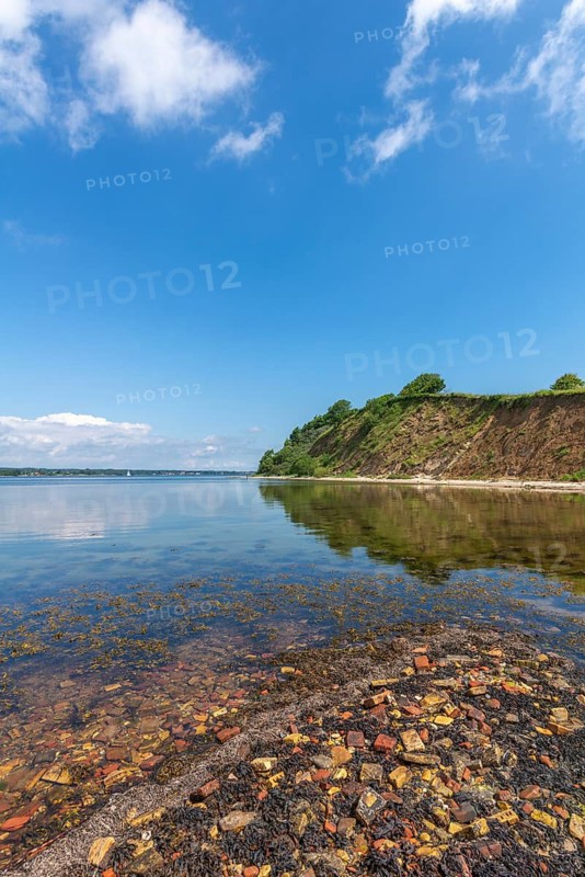 Steep coast with beach in the nature reserve Holnis peninsula on the Flensburg Fjord, NSG, bricks of the former brickworks on the shore, water reflection, blue sky, white clouds, Glücksburg, Schleswig-Holstein, Germany