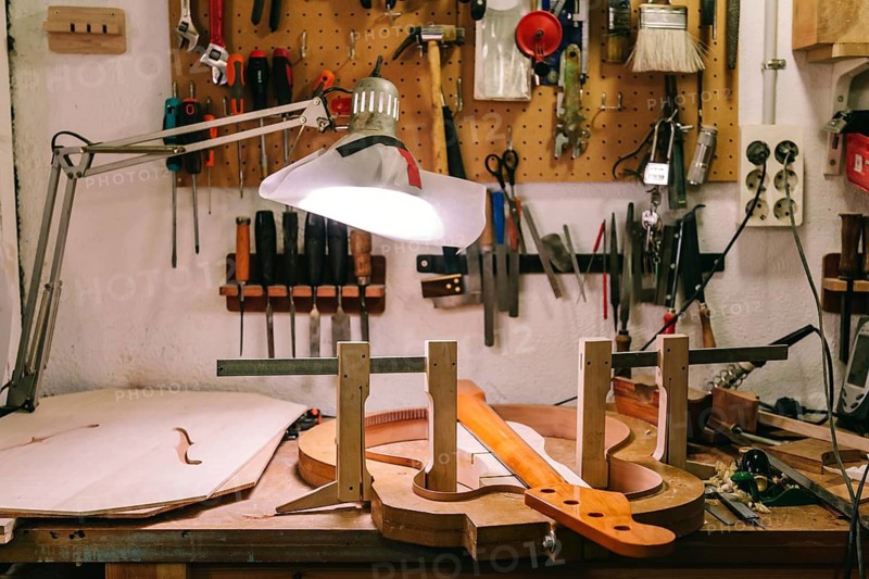 A detailed view of a luthier's workshop where a bass guitar is being meticulously crafted. Tools and materials are neatly arranged, reflecting precision and craftsmanship