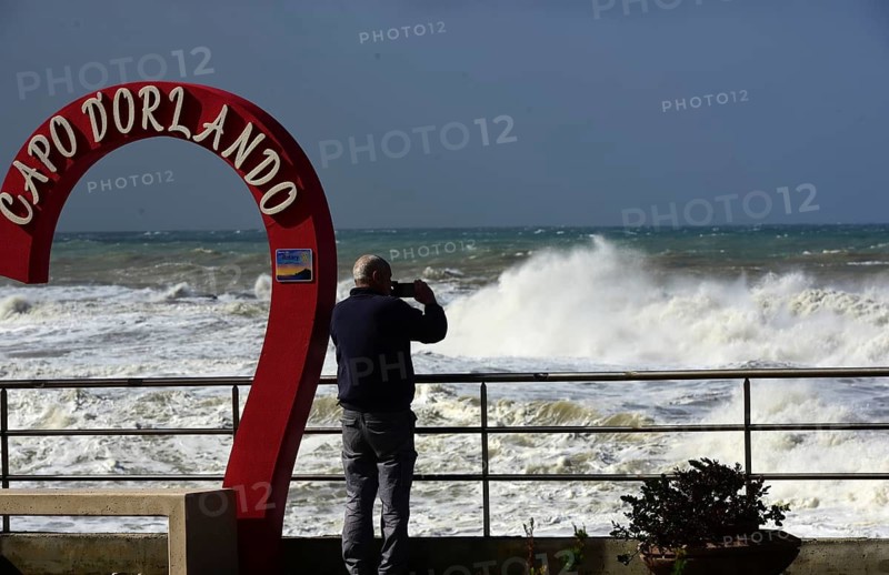 Severe weather waves on the quay wall of Capo D'Orlando. A person photographs the stormy sea on the waterfront