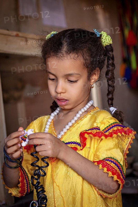 A girl in traditional yellow clothing looks at an object with concentration, Little girl from Algeria
