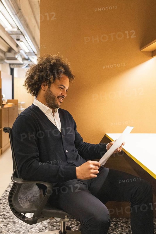 A man is seated at a desk in a modern coworking space, reviewing documents. The atmosphere is warm and professional, highlighting a collaborative work environment