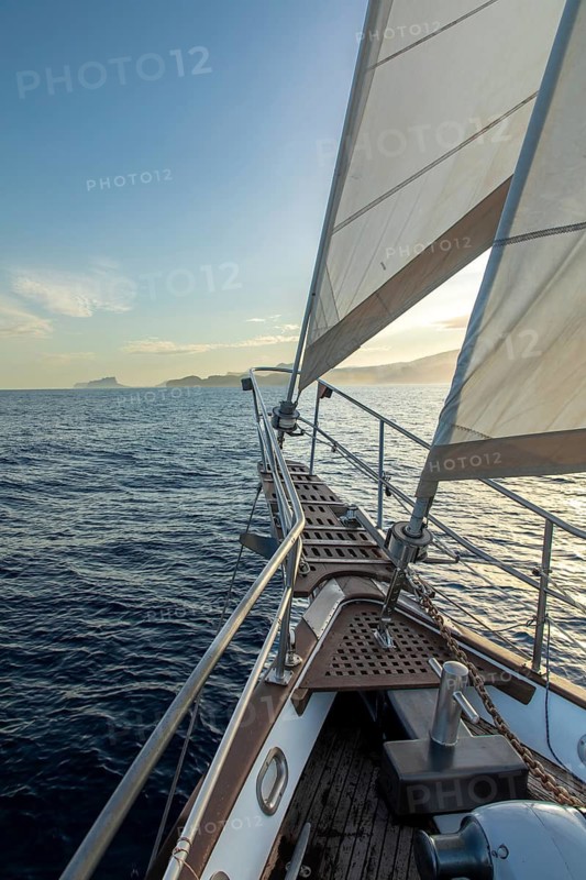 A tranquil scene of a sailboat navigating the calm waters of the Mediterranean Sea at sunrise, with the Costa Blanca shoreline silhouetted in the background