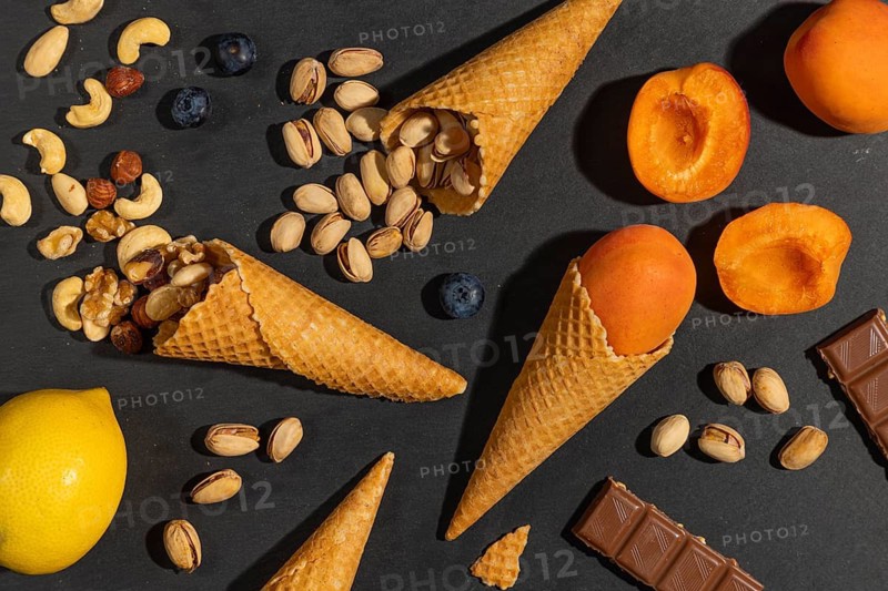 Lemon, nuts, apricots and chocolate pieces with ice cream cones on a black background