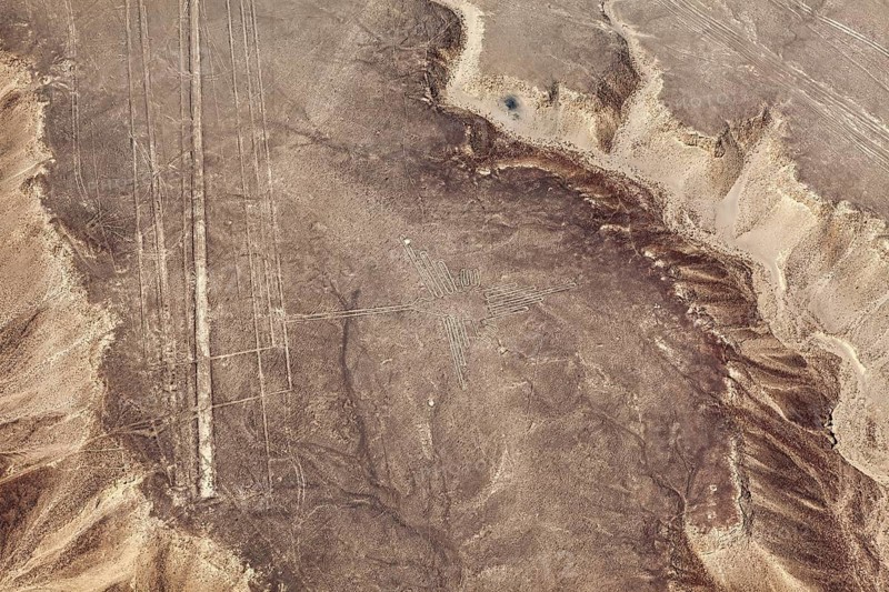Aerial view of a sandy area with visible patterns and lines, surrounded by sloping terrain, the geoglyphs and images in the desert near Nasca and Palpa in Peru