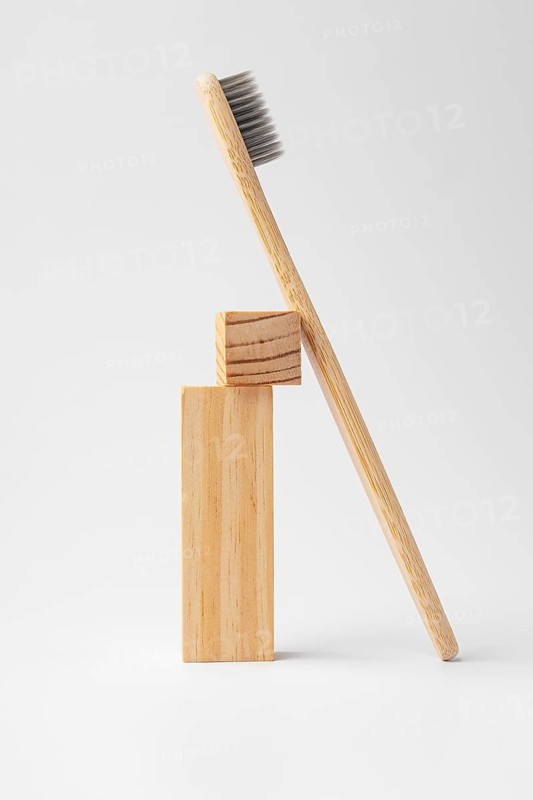 A natural bamboo toothbrush elegantly leans against two stacked wooden blocks. The minimalist design highlights eco-friendly materials against a light gray background