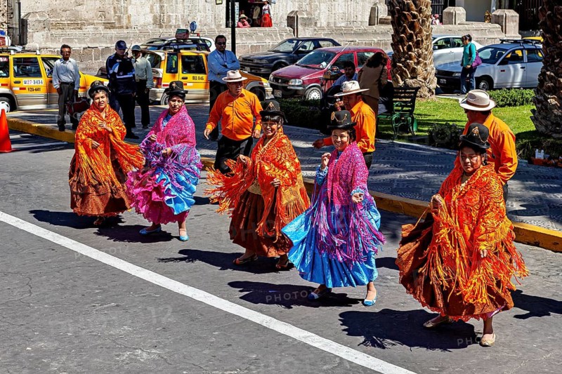 Women in traditional colorful clothes dance energetically on a busy street, a colorful dance and folklore group in Arequipa in Peru