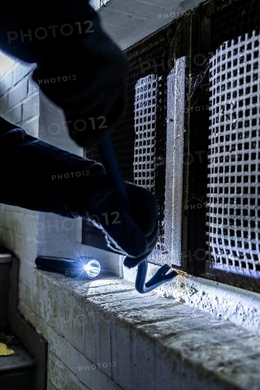 Symbolic image of a house burglary, perpetrator has approached a house from the garden side and tried to break open a cellar window to get into the flat
