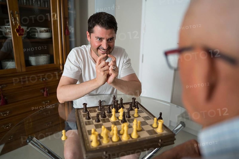 A cropped unrecognizable father and adult son engage in a thoughtful game of chess, fostering bonding and cherished family moments across generations in the comfort of their home