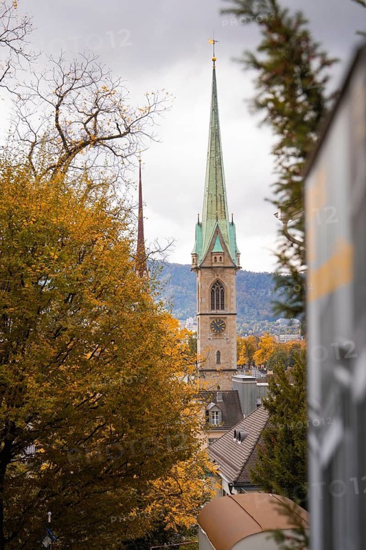 Pointed church tower in front of autumnal trees and cloudy sky, Zurich, Switzerland