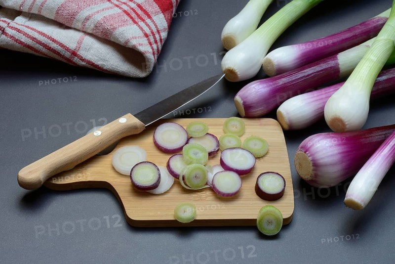 Spring onions and onion rings with a knife on a wooden board, spring onion