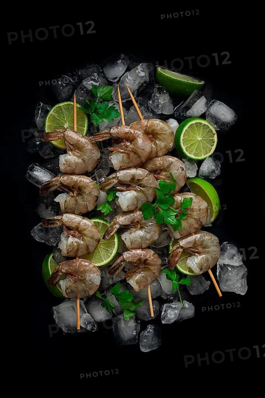 Frozen raw shrimp vannamey, on wooden skewers, ice cubes and lime slices, top view, no people