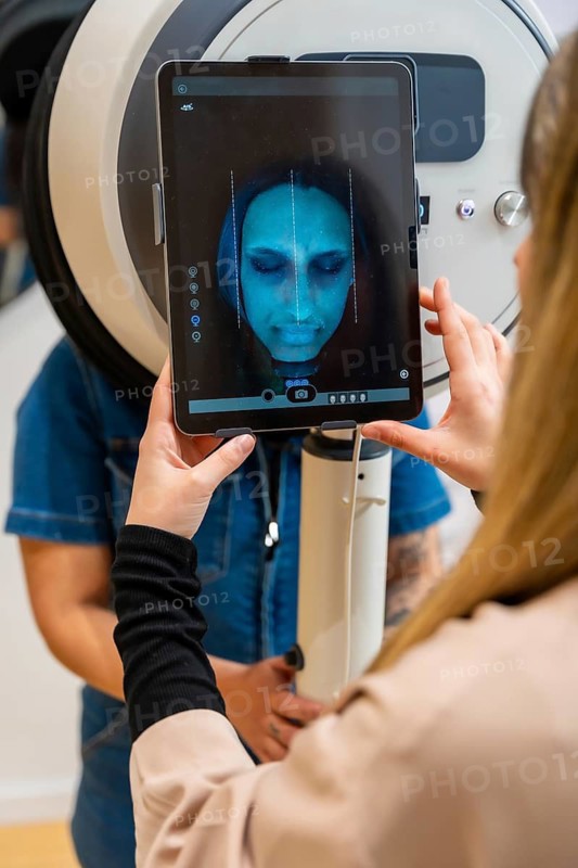 Specialist performing a detailed facial skin analysis on a female client using modern diagnostic technology to assess skin health and customize beauty treatments