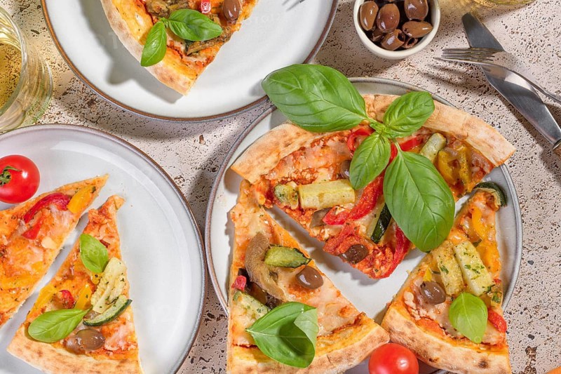 Rustic vegetarian pizza topped with fresh basil, zucchini, eggplant, peppers, and olives. Perfectly baked crust, vibrant and colorful, served on a ceramic plate