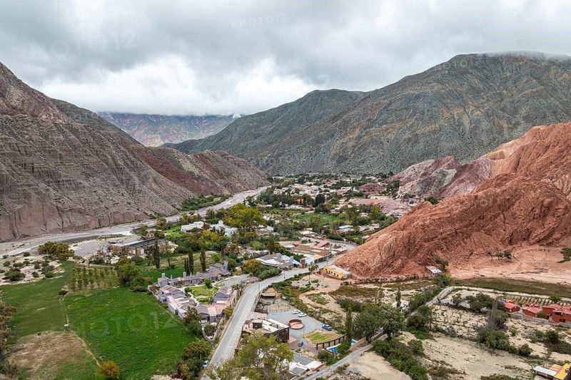 A breathtaking aerial view of Purmamarca in Jujuy, Argentina, showcasing the vibrant valley surrounded by colorful hills, lush greenery, and the charming village nestled below