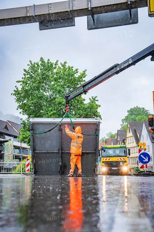 A worker in orange rain gear operates a lifting crane in a rainy street, Hermann Hesse railway construction site, Calw, Black Forest, Germany
