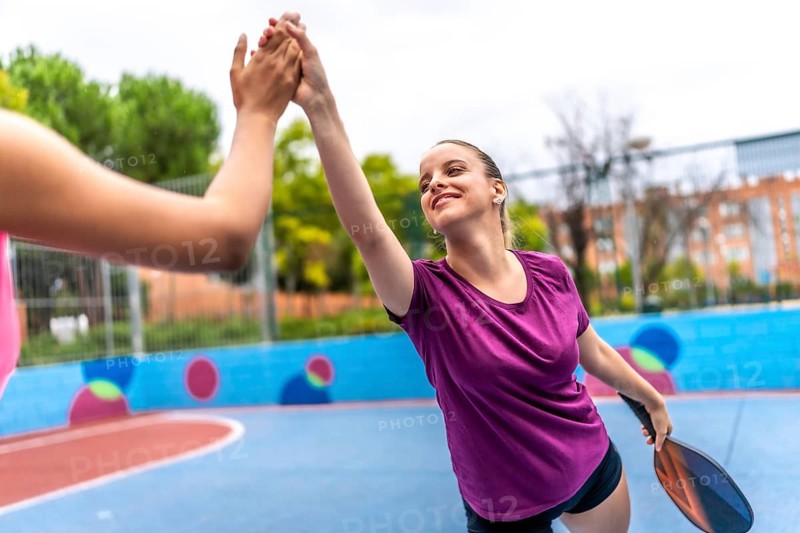 Multi-ethnic team of women high-fiving while celebrating as they play pickleball in an outdoor court