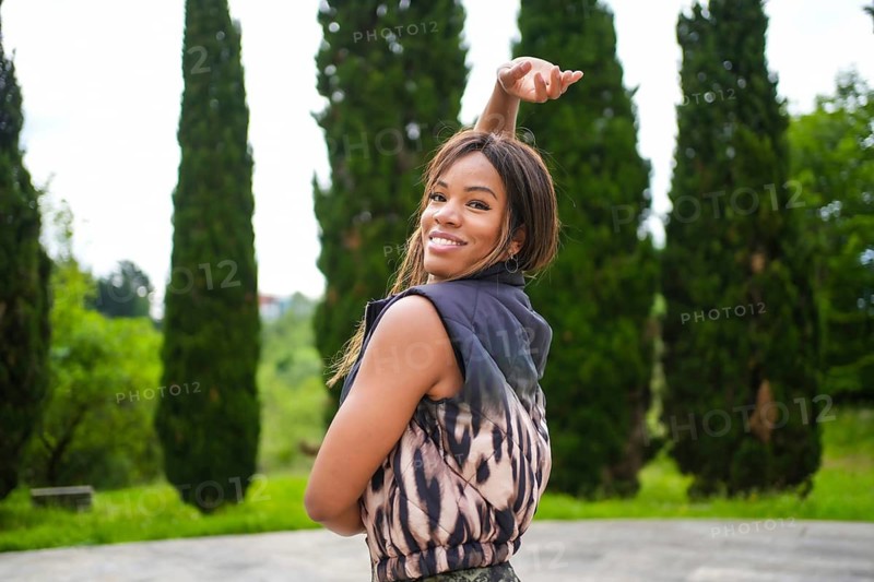 Powerful female latin smiling dancer raising the arm dancing salsa in a park