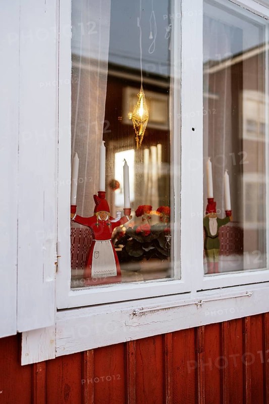 A cozy Lapland window adorned with traditional Swedish Christmas decorations, featuring red wooden figures, candles, and festive ornaments on display