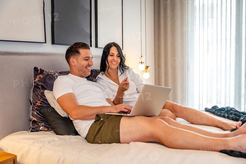 Tranquil scene of a couple lying on the bed using laptop together