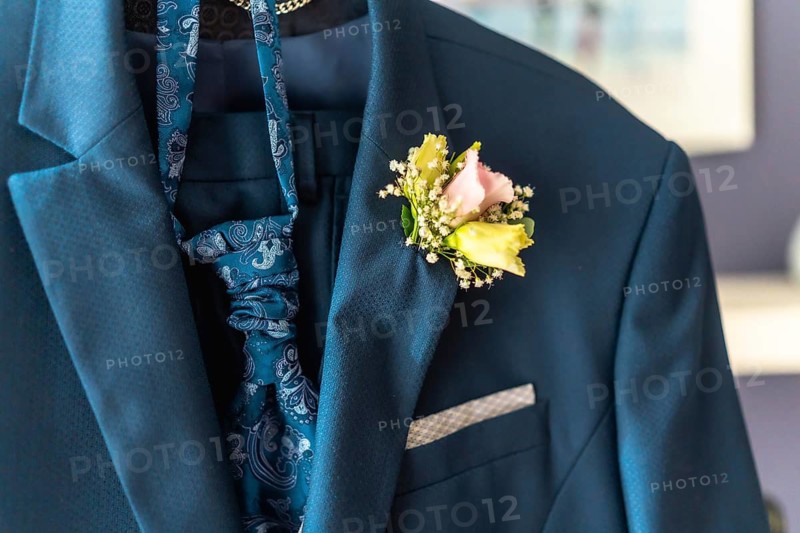 A man's blue suit jacket is adorned with a boutonniere of pink and yellow flowers