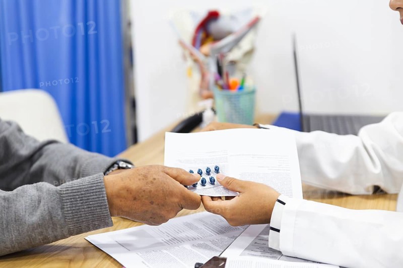 A close-up of a doctor and a patient exchanging medical information in a clinical setting. The patient hands over documents and medication, indicating a collaborative consultation