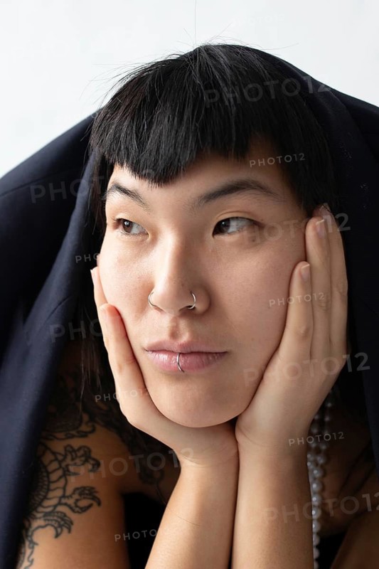 A close-up portrait of a young Asian woman with dark hair, bangs, and facial piercings