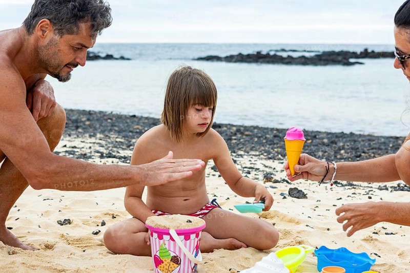 A little girl with Down syndrome enjoys a joyful day at the beach with her family Surrounded by sand toys and the ocean, she plays happily, creating cherished memories