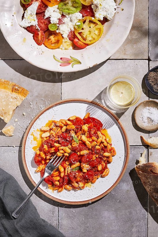 Top view of a homemade meal featuring freshly made pasta coated in a rich tomato sauce, complemented by a colorful tomato salad with varied heirloom varieties and fresh cheese