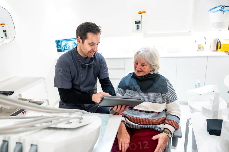 Dentist discussing treatment options with a senior patient while showing examination results on a tablet in a modern dental clinic