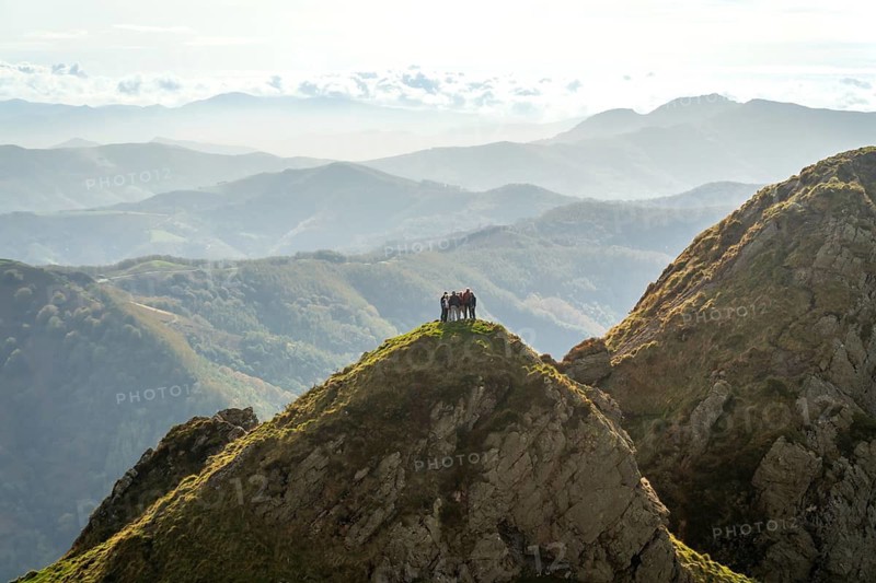 Hikers stand on the summit of aiako harria, part of the penas de aia mountain range, enjoying the panoramic view of the basque country landscape