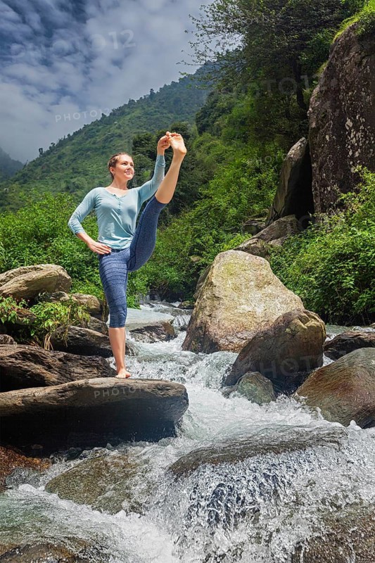 Yoga outdoors, woman doing Ashtanga Vinyasa Yoga balance asana Utthita Hasta Padangushthasana, Extended Hand-To-Big-Toe Pose position posture outdoors at waterfall