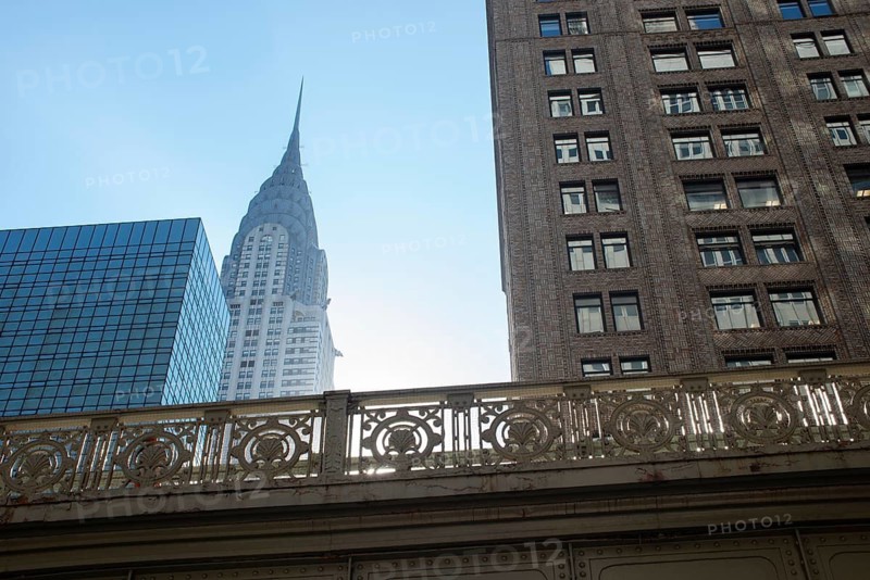 From below the iconic Chrysler Building, a classic example of Art Deco architecture in Manhattan, towers above an intricately designed iron bridge